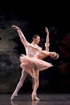 two ballerinas in pink tutu and white leotards, one holding the leg