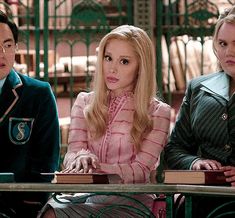 three people sitting at a table with books in front of them and one person holding a book