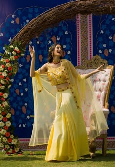 a woman in a yellow sari is standing on a stage with her arms outstretched