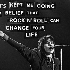 a man with his hand up in front of a microphone and some words on the wall behind him