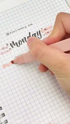 someone is writing on a piece of paper with a pink crayon marker in their left hand