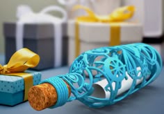 a wine bottle wrapped in blue string and tied with a yellow ribbon next to two gift boxes
