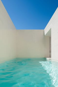an empty swimming pool with blue water in the middle and white walls on either side