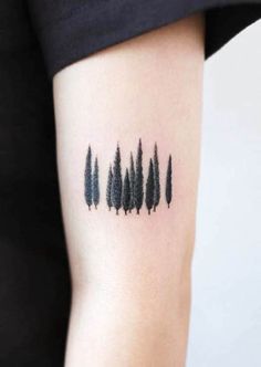 black ink tattoos on the arm of a woman's left arm, with trees in the background