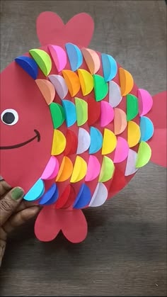 a hand holding up a paper fish made out of colored construction paper with hearts on it