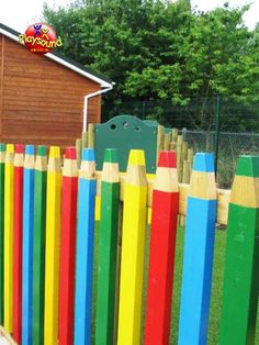 a wooden fence with colored pencils painted on it and a building in the background