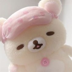 a white teddy bear with a pink hat on it's head and eyes closed