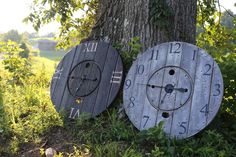 two clocks sitting next to each other on the ground near a tree and some grass