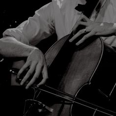 a black and white photo of a man holding a cello in his right hand, with the strings still attached