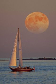 a sailboat floating in the ocean with a full moon rising over it's horizon