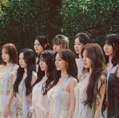 a group of young women standing next to each other in front of trees and bushes