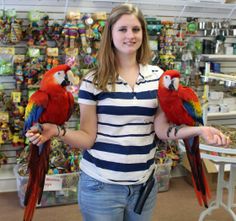 a woman holding two red and yellow parrots in her hands while standing next to a store shelf