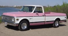 a pink and white truck parked next to the water