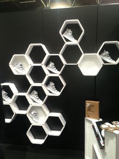 an exhibit with shelves and shoes on display in front of a black wall that has white hexagons attached to it
