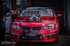 a red car parked in front of a man with an engine on it's hood