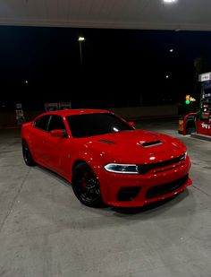 a red dodge charger parked in front of a gas station at night with its lights on