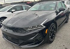 the front end of a black car in a parking lot with other cars behind it