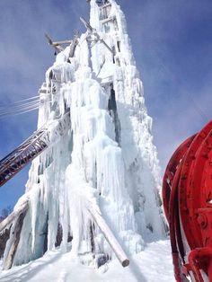 a very tall ice covered mountain next to a red fire hydrant in the snow