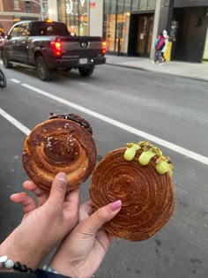 a person holding two pastries in their hands on the side of the road with cars behind them