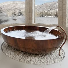 a large wooden tub sitting in front of a window next to a snow covered mountain