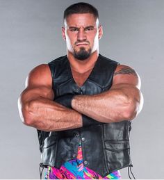a man with his arms crossed wearing a leather vest and multicolored shorts is posing for the camera