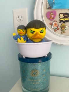 two rubber ducks are sitting in a bowl on a counter next to a wall light