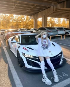a woman sitting on top of a white car in the middle of a parking lot