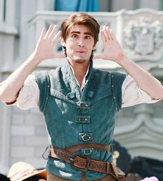 a man with his hands in the air while wearing a green vest and brown pants