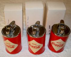 three coca - cola cans sitting next to each other in front of two boxes on a bed
