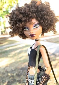 a close up of a doll wearing a dress and holding a handbag in the park