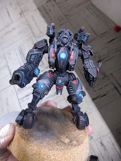 a person holding up a toy robot on top of a rock