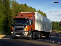 an orange semi truck driving down the road with trees in the backgrouund