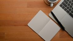 an open laptop computer sitting on top of a wooden table next to a cup of coffee