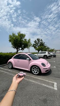 a pink car parked in a parking lot next to a person holding a cell phone
