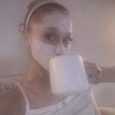 a woman is drinking from a cup while wearing a white towel on her head and face