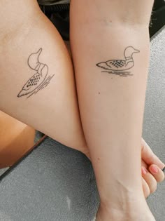 two tattoos on the legs of people who are sitting next to each other, one with a duck and another with a paddle