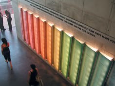 two women walking past a wall with colorful panels on it's sides and people standing around