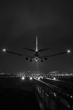 an airplane is flying low over the city at night with its lights on and it's landing gear down