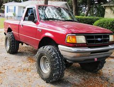 a red pick up truck parked in front of a house with large tires on it
