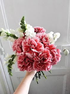 a hand holding a bouquet of flowers in front of a white door with pink and white carnations