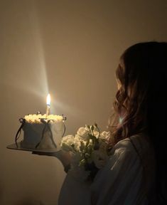 a woman holding a cake with a candle on it and flowers in front of her