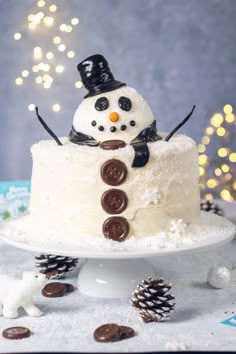a snowman cake sitting on top of a table next to pine cones and christmas decorations