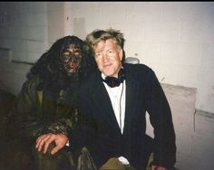 two people dressed up as zombies sitting next to each other in front of a wall