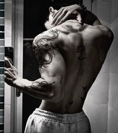 a man with tattoos on his back taking a selfie in front of a mirror