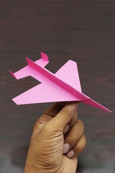 a hand holding a pink origami airplane