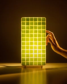 a hand is touching the back of a green square light that has squares on it