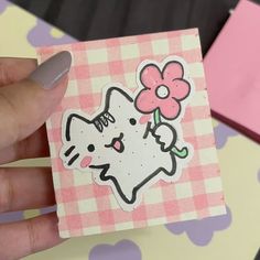 a hand holding a piece of paper with a cat and flower sticker on it
