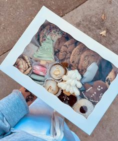 a person holding up a box filled with assorted cookies and pastries in front of their face
