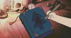 a hand holding a pen writing on a blue book next to skulls and other items