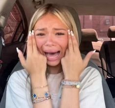 a woman sitting in the back seat of a car with her hands on her face